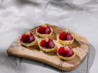 Elegant raspberry tarts on wooden board