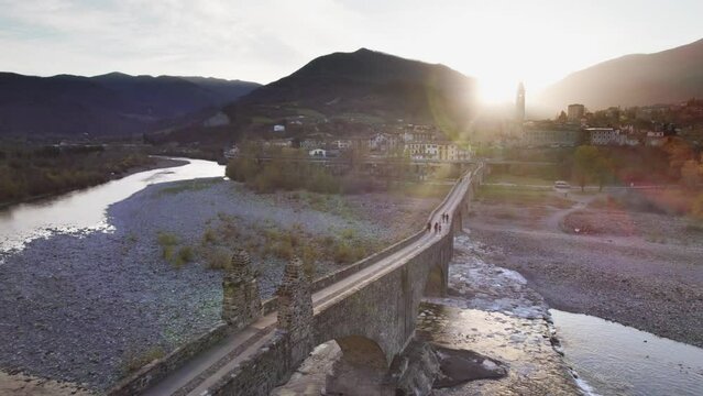 Reveal aerial shot over Gobbo bridge over Trebbia river during sunset, Bobbio, Piacenza province, Emilia Romagna, Italy. 