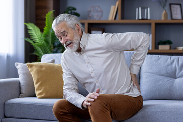 Senior man experiencing back pain while sitting on sofa