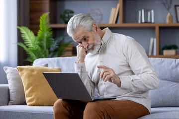 Senior man with beard using laptop on a comfortable sofa at home