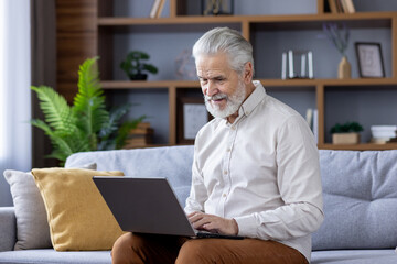 Senior man using laptop on cozy sofa at home