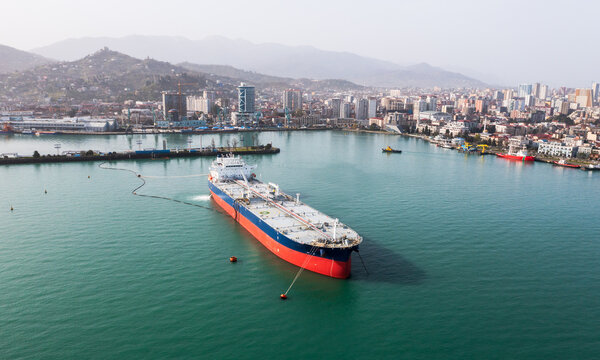 Aerial view of tanker ship in clear turquoise waters near coastal cityscape.