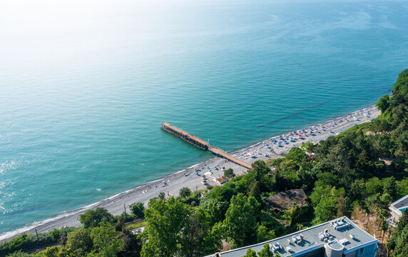 Aerial view of serene beach with long pier, azure waters, and vibrant beachgoers dotting shoreline.