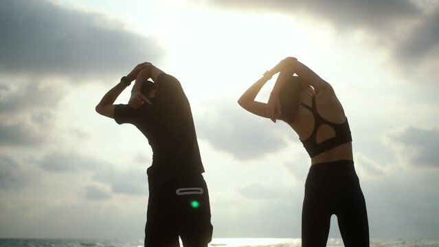 Back side couple young two friends stretching arm before running at seaside. Young couple wearing sportswear running on sand sea ocean beach outdoor jog on seaside. Training athlete work out outdoor.
