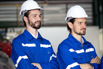 Group of people wear safety helmets and blue jackets standing in factory. Young adult beard man...