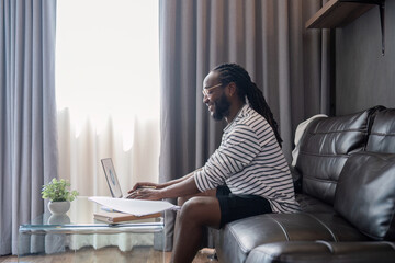 African American man working with laptop computer remote while sitting at sofa in living room....