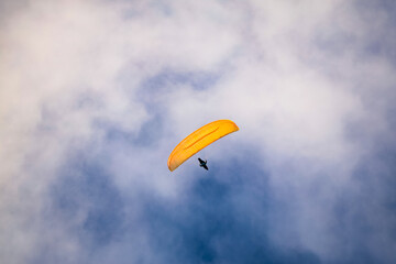 Paragliding extreme sport. Photo with a sportsman while practicing paragliding. Blue sky white clouds background.