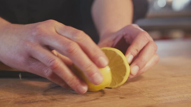 Close up of woman's hands cutting whole fresh lemon in half on a wooden board with a steel knife. Bright kitchen, studio shot. High quality 4k footage
