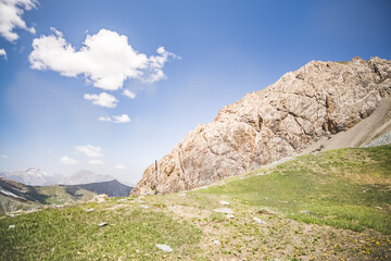 Panoramic landscape in the mountains with rocks and scree, with grass glades, snow and glaciers on a sunny summer day in the Fann Mountains in Tajikistan with mountain ranges