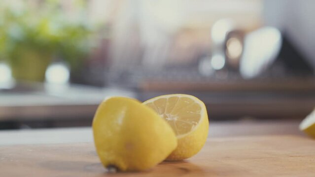 Close up of woman's hands cutting whole fresh lemon in half on a wooden board with a steel knife. Bright kitchen, studio shot. High quality 4k footage
