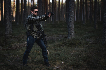 Private military soldier with pistol, assault rifle and body armor in the twilight forest.