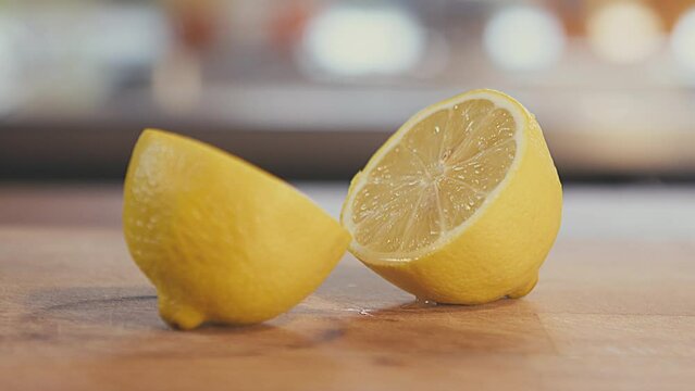 Close up of lemon fruit cut in half lying on a wooden table. Slow motion studio shot. Brightly lit. Defocused kitchen in the background. High quality 4k footage