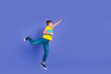 Fototapeta na wymiar Photo of glad funky boy wear stylish yellow clothes raise fist hand run fly air look empty space isolated on violet color background