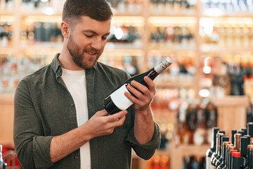 Reading information on the bottle. Man is choosing wine in the store