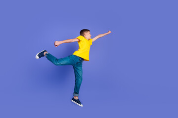Fototapeta na wymiar Full length photo of cheerful funny glad boy wear trendy yellow clothes fly air jump up empty space isolated on violet color background