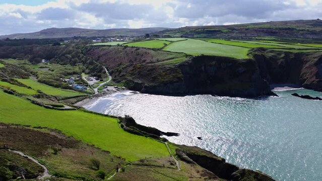 Aerial shot tracking and panning towards a sheltered cove and beach in West Wales near Fishguard