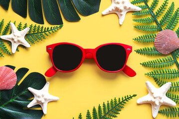 Summer holidays.Top view of red sunglasses, starfish, seashells,monstera leaf and tropical palm leaves. Summer vacation concept