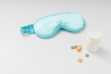 Sleep mask and vitamins for relaxation on white desk. Empty space