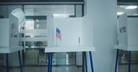 Dolly shot of voting booths with American flag logo in light polling station office. National...
