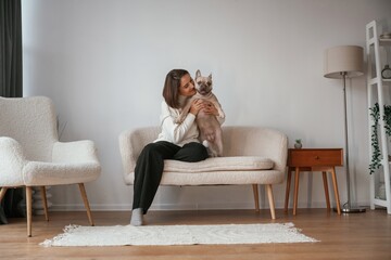 Front view, sitting on the little sofa. Young woman is with her pug dog at home