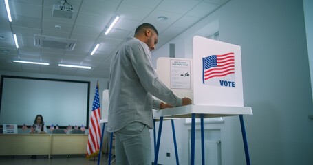 African American male voter walks for registration table at polling station, takes paper ballot....
