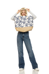 Beautiful young happy blonde woman in jeans with beach bag on white background