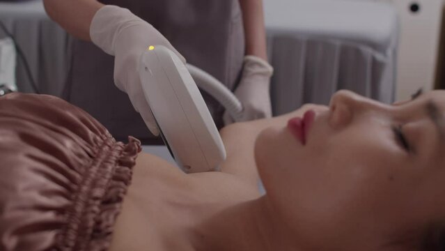 Cropped shot of female Asian client receiving underarm laser epilation from beautician in spa salon