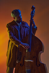 Man in retro flat cap playing double bass with vibrant blue and orange neon light against gradient...