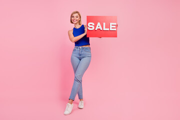 Full size photo of pretty young woman hold sale card empty space wear blue top isolated on pink...