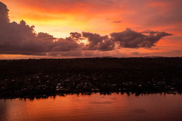 Scene of colorful sunset sky with clouds over evening city. Photo view from drone from the sea.