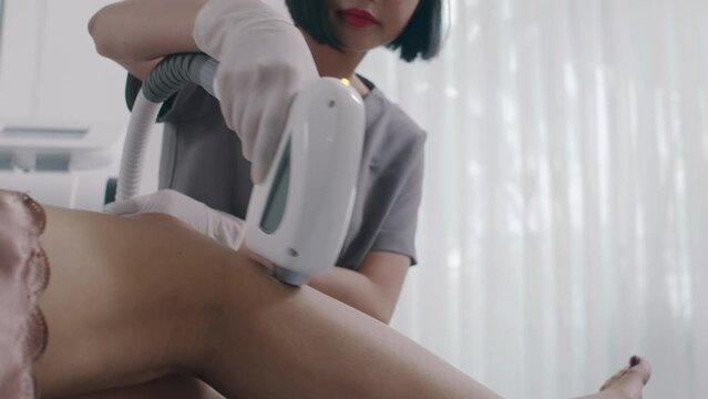 Cropped shot of young cosmetologist giving laser epilation treatment to client getting procedure on legs