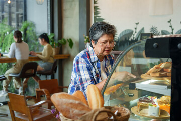 Mature woman in checkered shirt peers into display case at various breads, intense focus on selection, backdrop of customers in cozy cafe corner, invoking local bakery charm........