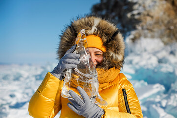 Happy woman wearing winter yellow jacket holding piece of transparent crushed ice cubes over her...