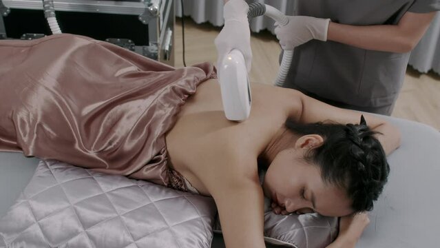 High angle of young female client attending back laser hair removal procedure in beauty salon