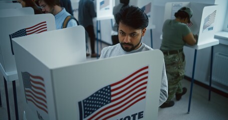 Indian man, American citizen votes in booth in polling station office. National Election Day in the United States. Political races of US presidential candidates. Civic duty and patriotism. Dolly shot.