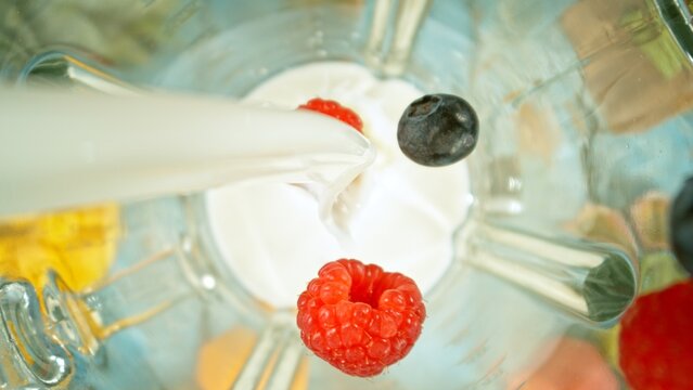 Freeze motion of mixing pieces of berries in blender with milk, top shot