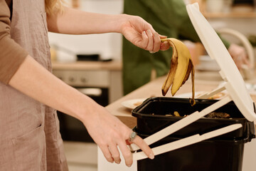 Side view of hands of young housewife opening lid of plastic bucket with compost and throwing...