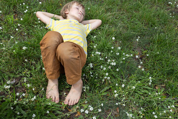 barefoot boy lies on the grass in the park. positive carefree childhood. Hello summer. relax,...