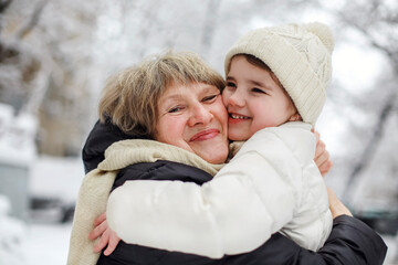 Loving grandmother with little girl granddaughter on snowy weather outdoors, smiling senior woman...