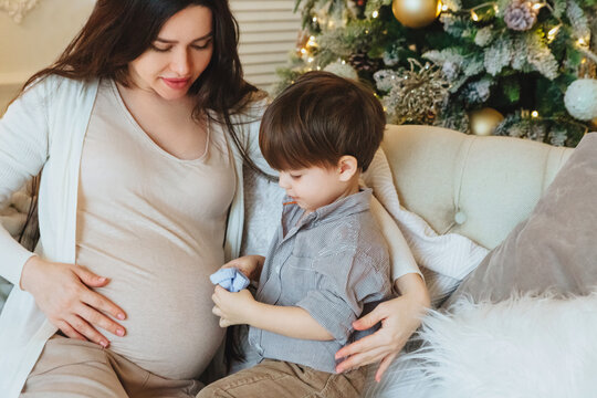 Young pregnant mother and little son toddler near xmas tree on Christmas morning at home