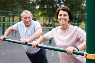 Elderly man and woman doing exercises in sports bars on outdoor sports ground