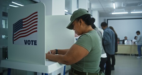 Female American army soldier votes in booth in polling station office. National Elections Day in the United States. Political races of US presidential candidates. Concept of civic duty. Dolly shot. - obrazy, fototapety, plakaty