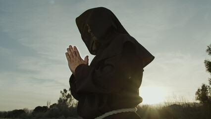 Silhouette Of A Monk Stands Praying On The Nature - obrazy, fototapety, plakaty
