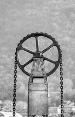 One round metal wheel of a lifting mechanism with a chain. Black and white vertical photo