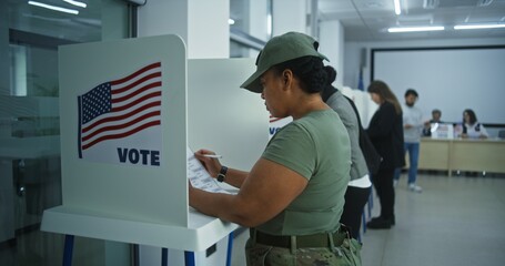 Female American army soldier votes in booth in polling station office. National Elections Day in...