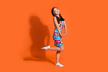 Full length photo of adorable nice pleasant woman dressed flower print clothes posing on one leg isolated on orange color background