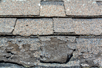 Close view of weathered shingles with a layer curled and damaged from the sun.