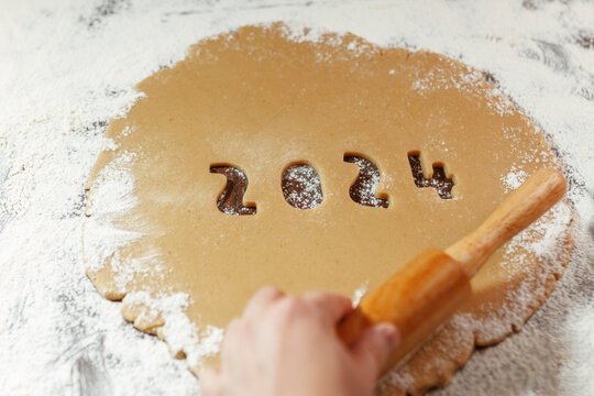 raw dough with 2024 numbers cut from rolled cookie on flour with woman's hand