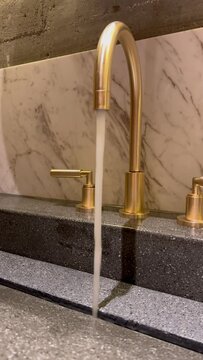 Tap water faucet in gold color: a powerful water pressure pours. Turned on the tap: a jet of water with a powerful pressure pours from tap. Accessories for the bathroom: a metallic golden faucet
