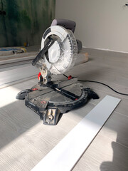 The miter saw or a multi material construction saw on the floor of the apartment with tape measure and wood. Renovation of the house